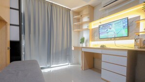 A modern hotel room with a bed, a desk with a TV, and a window with curtains. - Homey And Comfortable Studio Apartment At Daan Mogot City (Jakarta)