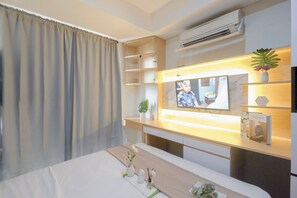 Una camera d'albergo con un letto, una TV a parete, uno scaffale con una pianta e un tavolino con un vaso.