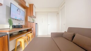 A modern living room with a brown sofa, wooden TV stand, and yellow stools. - Comfort Stay 1Br With Extra Room At Bassura City Apartment (Jakarta)