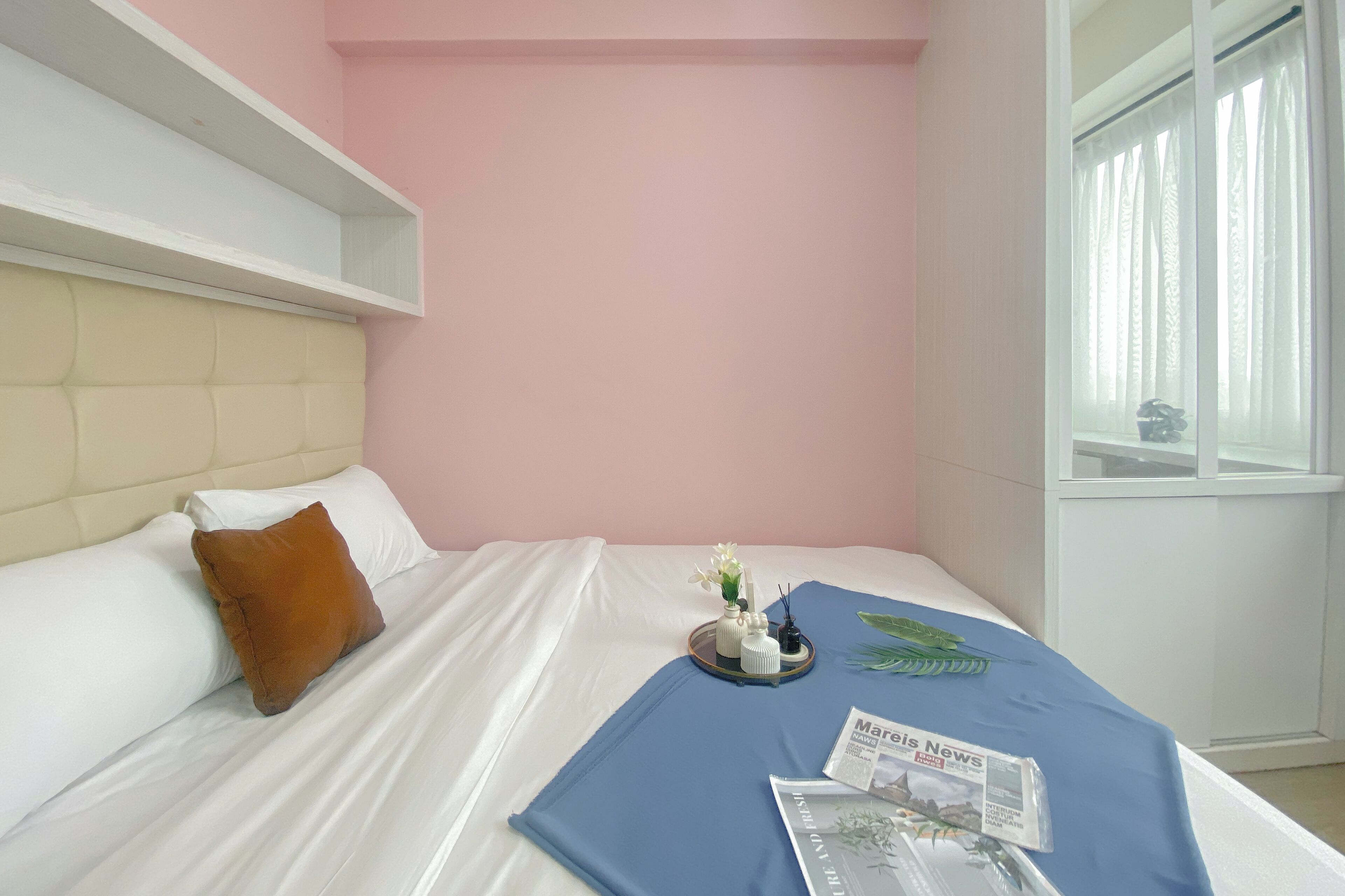A neatly made bed with a white headboard, a brown pillow, and a blue blanket. There is a tray with a vase of flowers and a magazine on the bed.