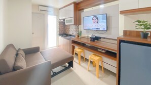 A modern kitchen with a flat-screen TV, a sofa, and two stools. - Comfort Stay 1Br With Extra Room At Bassura City Apartment (Jakarta)
