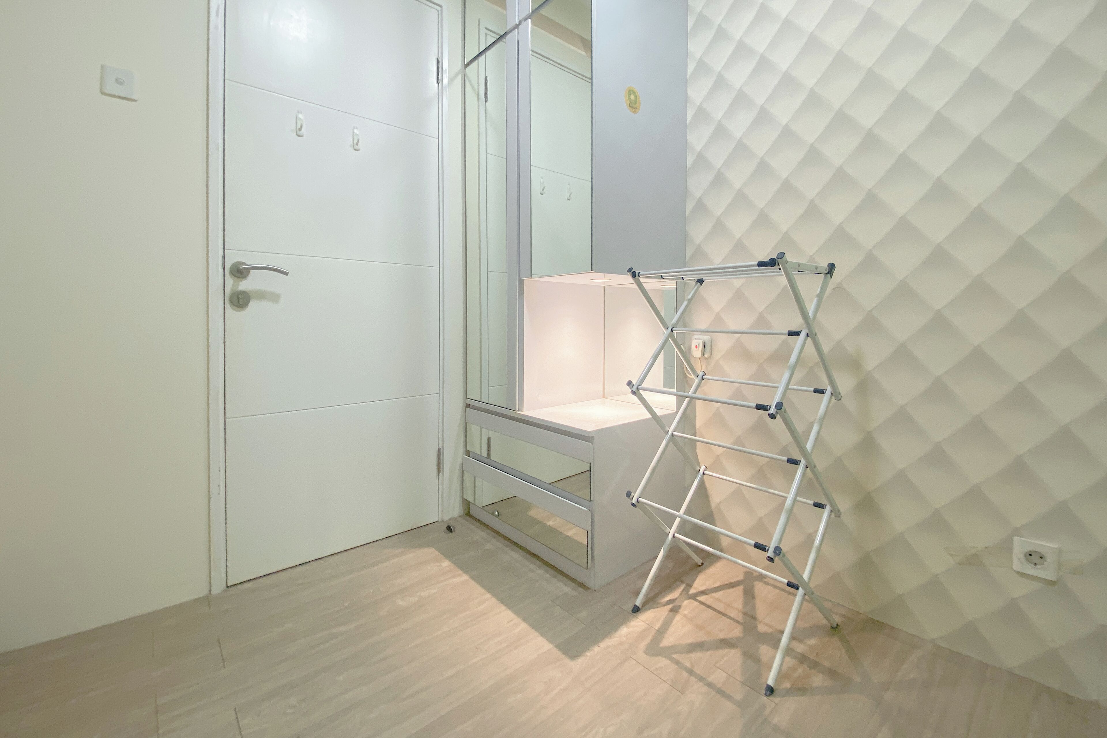 Een kamer met een witte kast, een glazen deur, een witte stoel en een metalen rek tegen een gestructureerde muur.