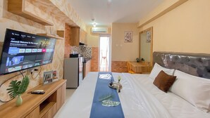 A hotel room with a bed, a TV mounted on the wall, a small kitchen area, and a bathroom visible through an open door.