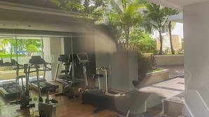 A gym with various exercise equipment, including treadmills and elliptical machines, and a view of palm trees and greenery outside.
