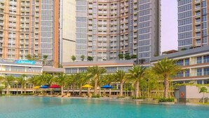 A modern hotel with a large pool area, palm trees, and a sign for 'Outdoors'. - Brand New And Homey Studio At Gold Coast Apartment Pik (Jakarta)