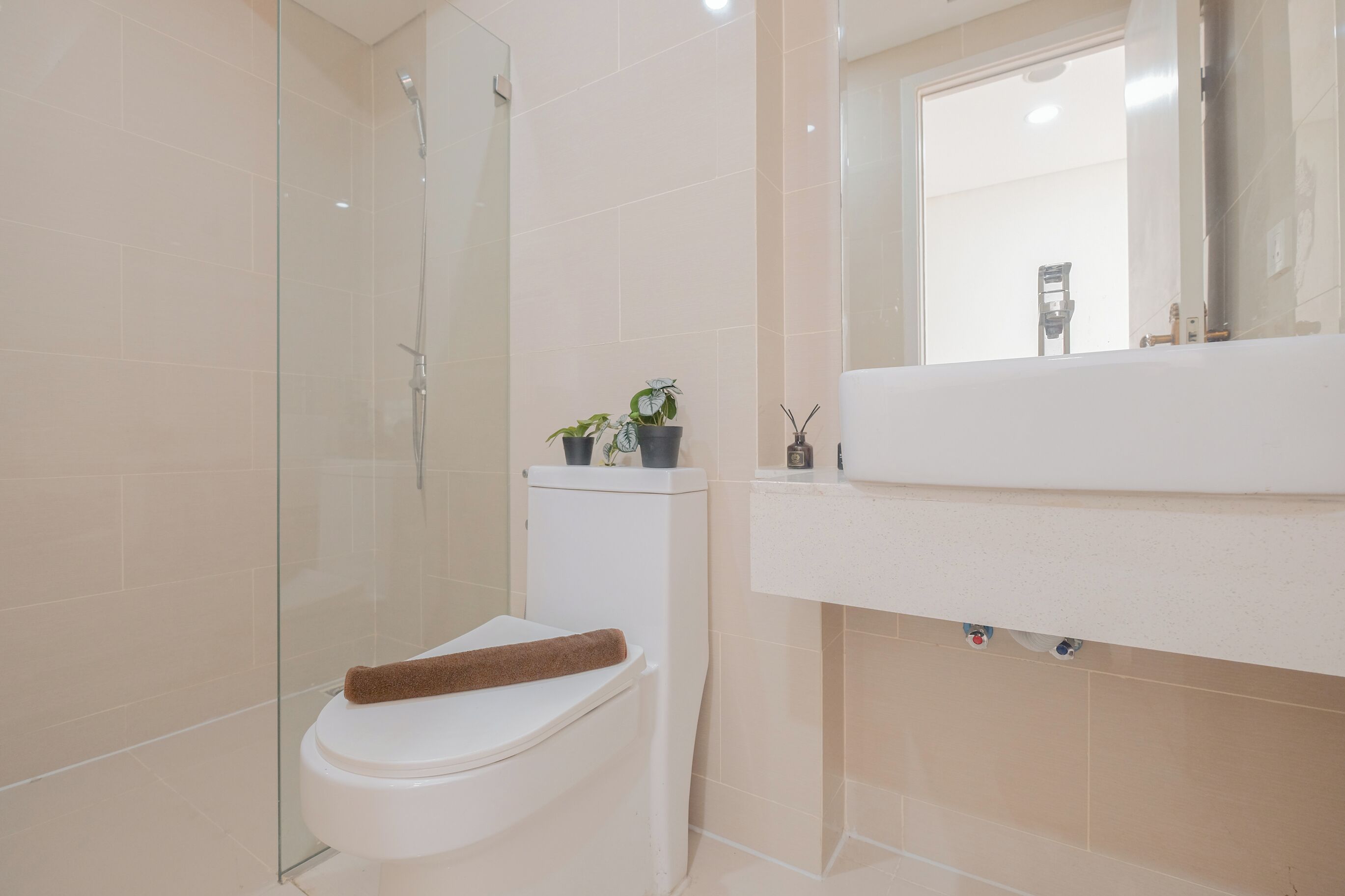 A modern bathroom with a glass-enclosed shower, a white toilet, and a sink with a mirror above it.