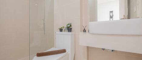 A modern bathroom with a glass-enclosed shower, a white toilet, and a sink with a mirror above it.