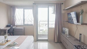 A hotel room with a bed, desk, chair, and a balcony with curtains. - Good Choice and Comfy Studio Apartment at LRT City Jatibening (Bekasi)