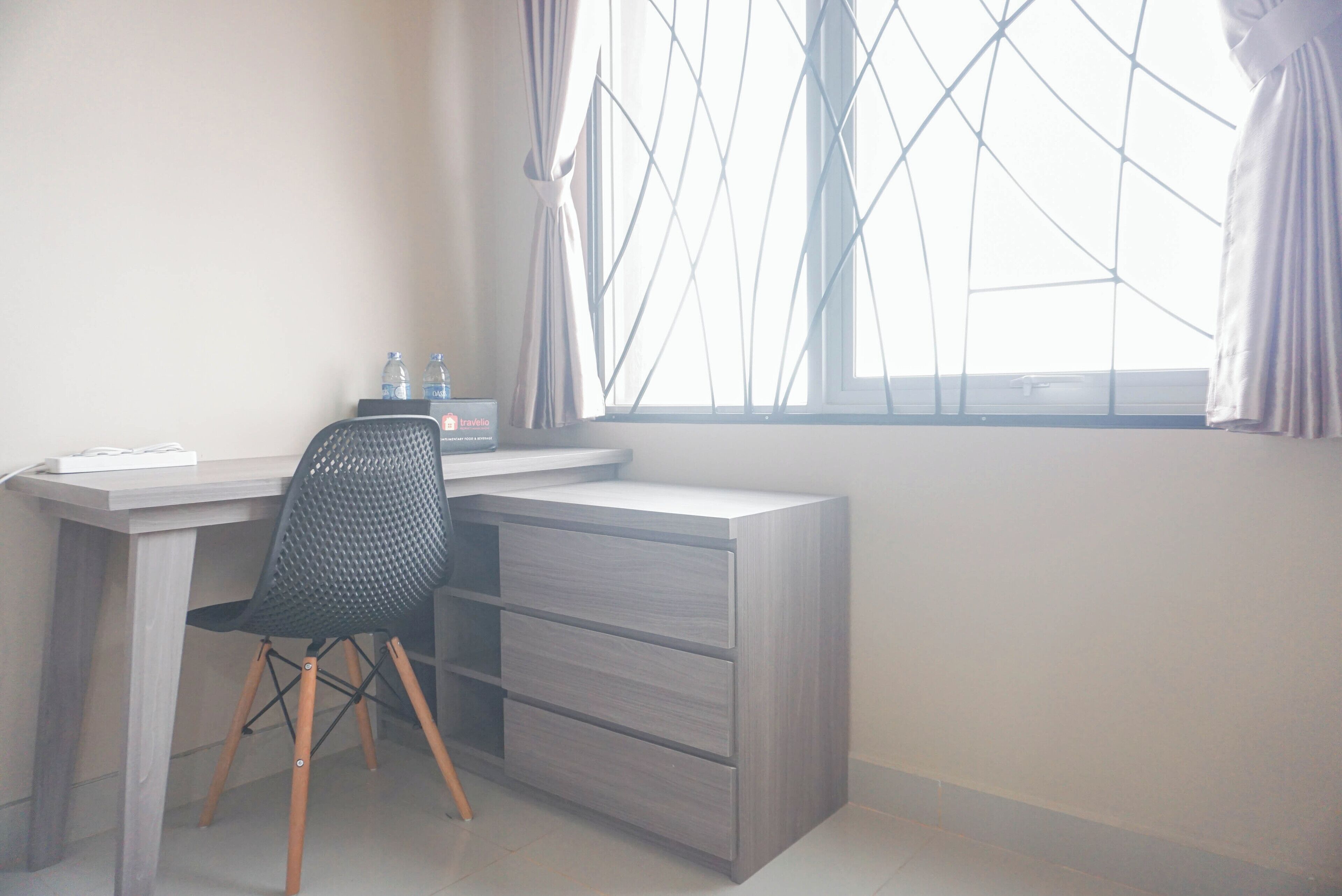 Une petite pièce bien éclairée, avec un bureau, une chaise et une fenêtre avec des rideaux.
