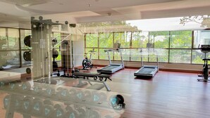 A gym with cardio equipment, weightlifting stations, and large windows offering a view of greenery. - Good Choice and Comfy Studio Apartment at LRT City Jatibening (Bekasi)