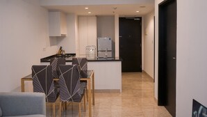 Cocina moderna con armarios blancos, encimera negra y refrigerador integrado. Hay una zona de comedor con una mesa y sillas.