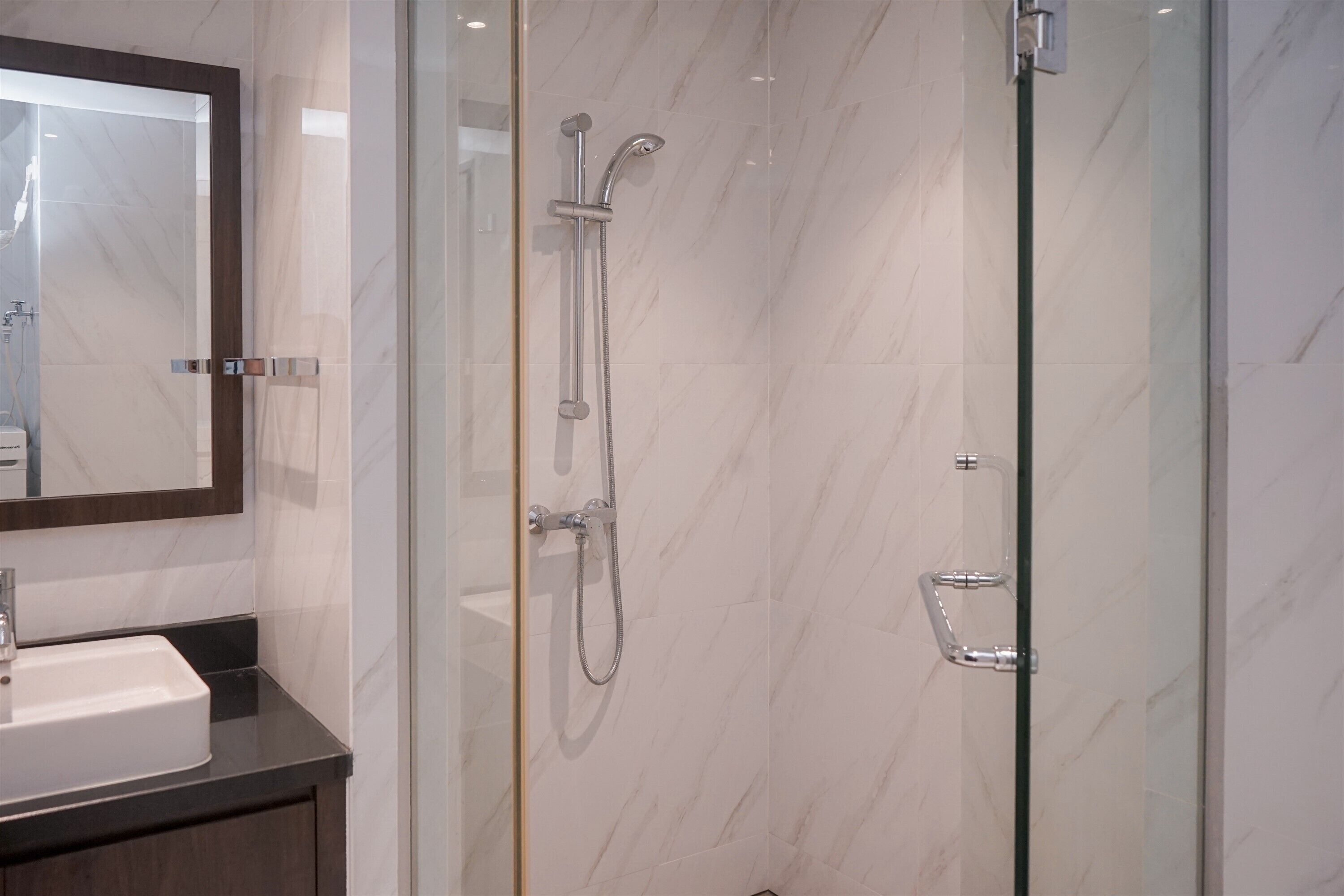 A modern bathroom with a glass shower enclosure, a marble-tiled wall, and a dark countertop with a sink.
