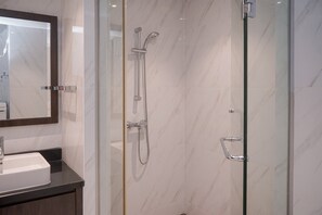 Un baño moderno con cabina de ducha de vidrio, pared con azulejos de mármol y encimera oscura con lavamanos.