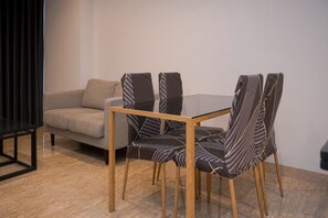 Una sala de estar moderna con una mesa de centro de vidrio, cuatro sillas a rayas y un sofá gris.