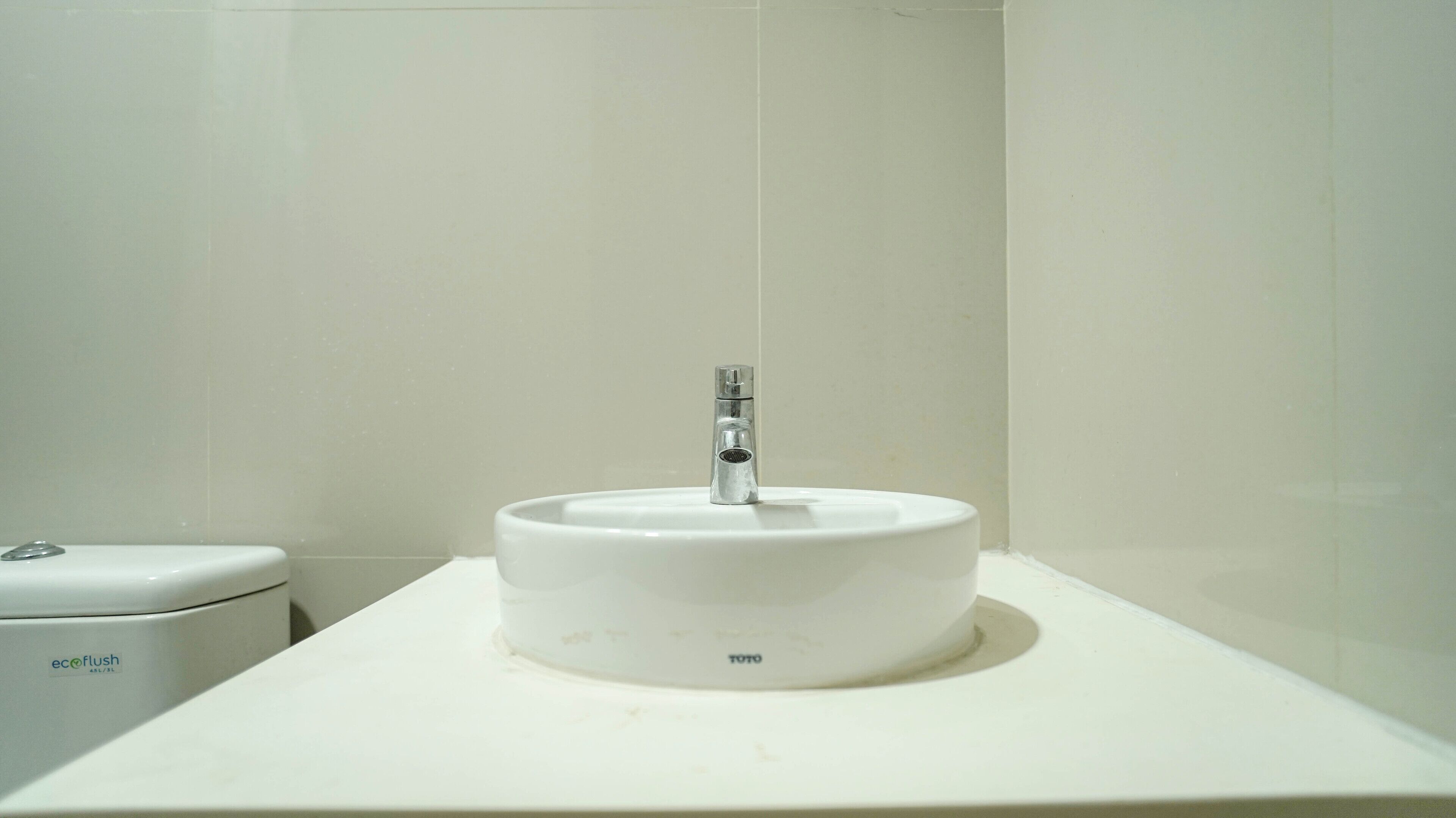A bathroom with a white sink, a toilet, and a wall-mounted faucet.