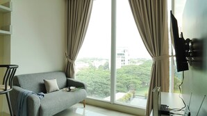 A modern living room with a grey sofa, a flat-screen TV mounted on the wall, and a large window with curtains.