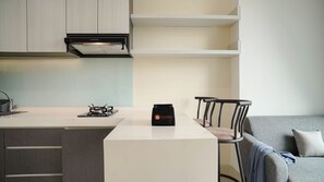 A modern kitchen with a built-in stove, a small island, and a seating area with a grey sofa and two chairs.