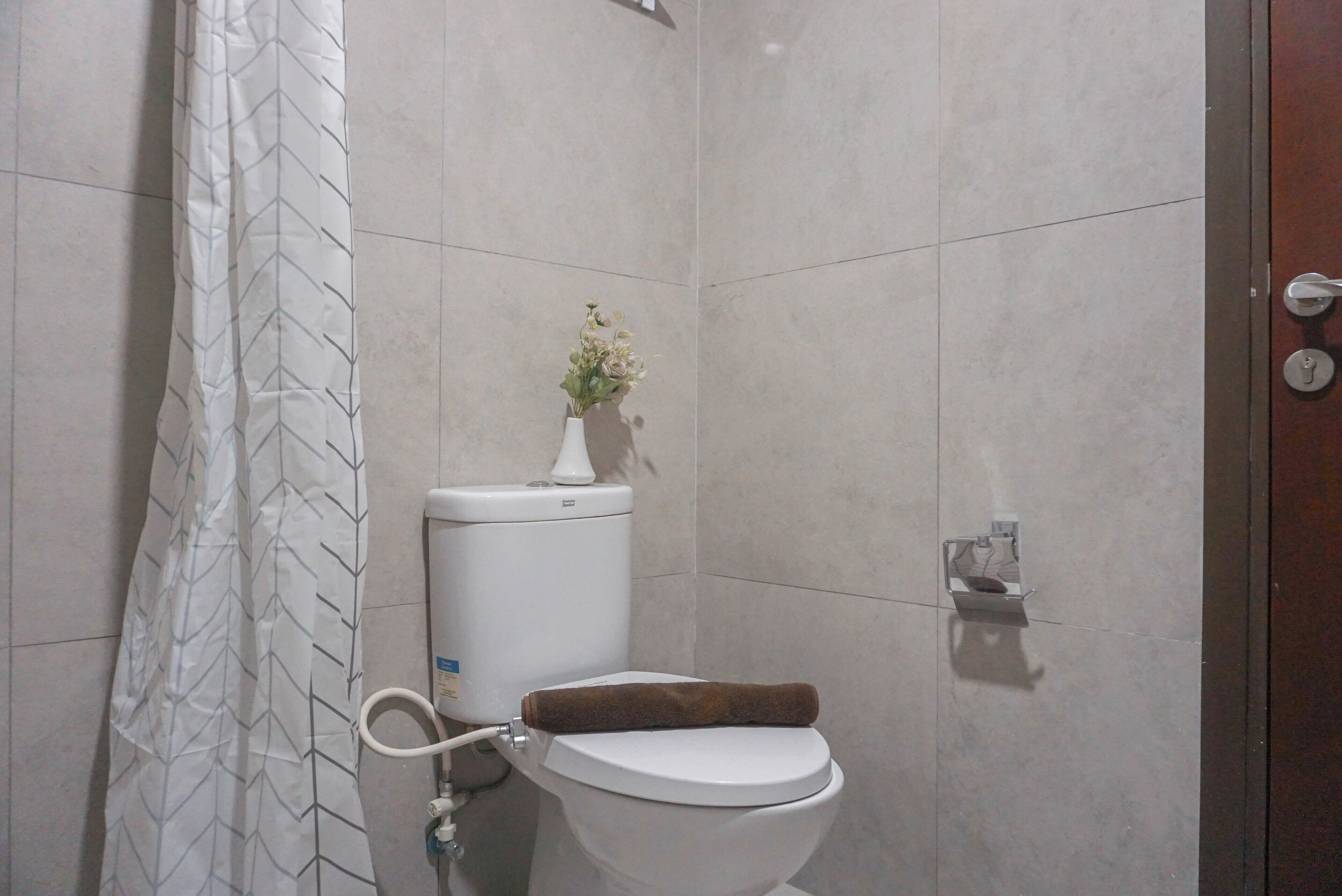 A bathroom with a toilet, a shower curtain, and a small vase with flowers on the wall.
