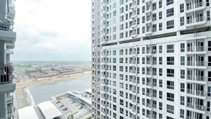 A high-rise building with multiple balconies and a view of a river and construction site below.
