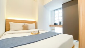 A neatly made bed with a wooden headboard, a grey blanket, and a small tray with a bottle and glasses.