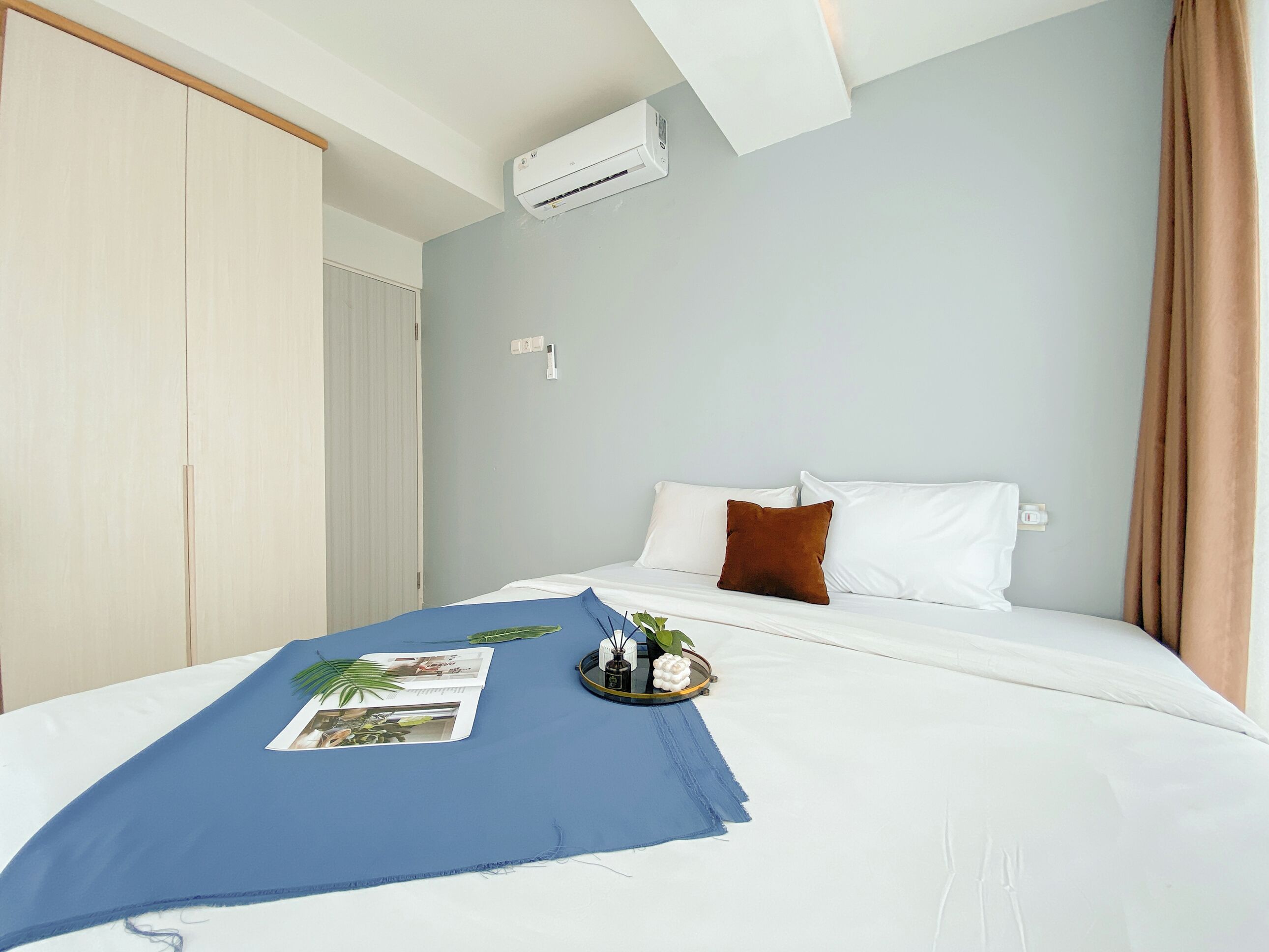 Ein Hotelzimmer mit einem Bett, einer blauen Tagesdecke, einem braunen Kissen und einem kleinen Tisch mit Blumen.