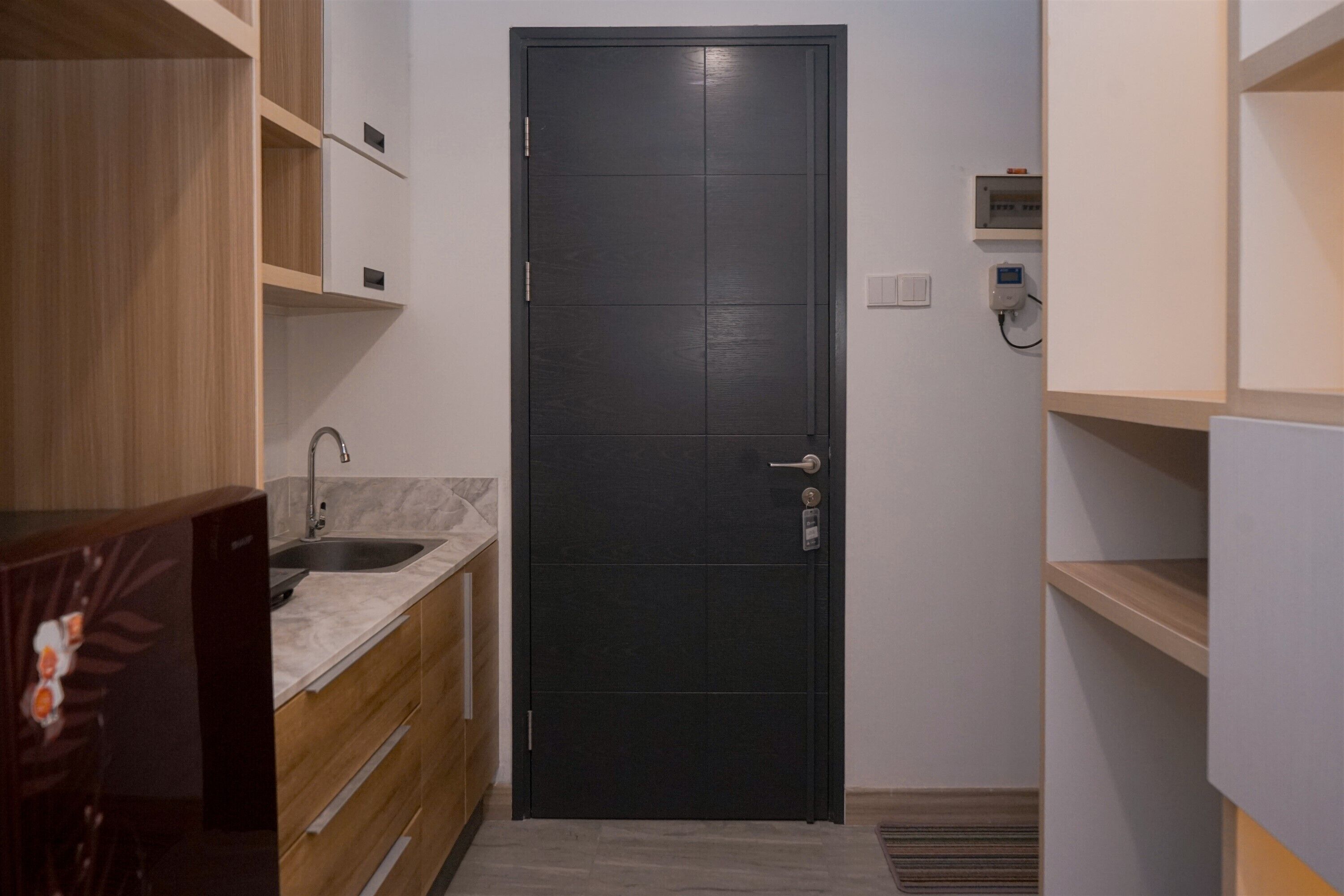 A small, modern bathroom with a dark door, a sink, and wooden cabinetry.