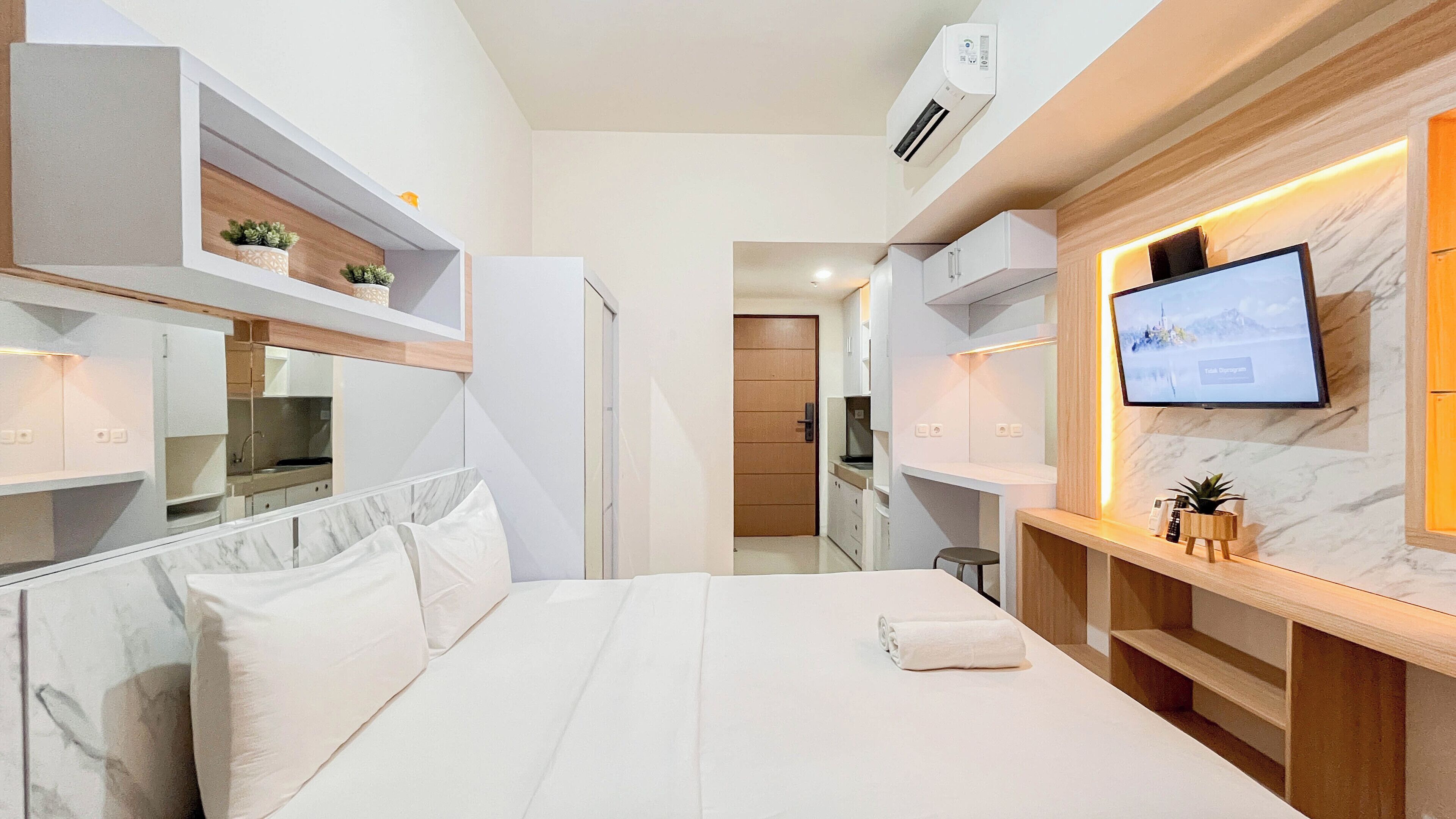 Une chambre d’hôtel avec un lit, un téléviseur fixé au mur, un petit coin cuisine et une salle de bain visible à travers une porte ouverte.