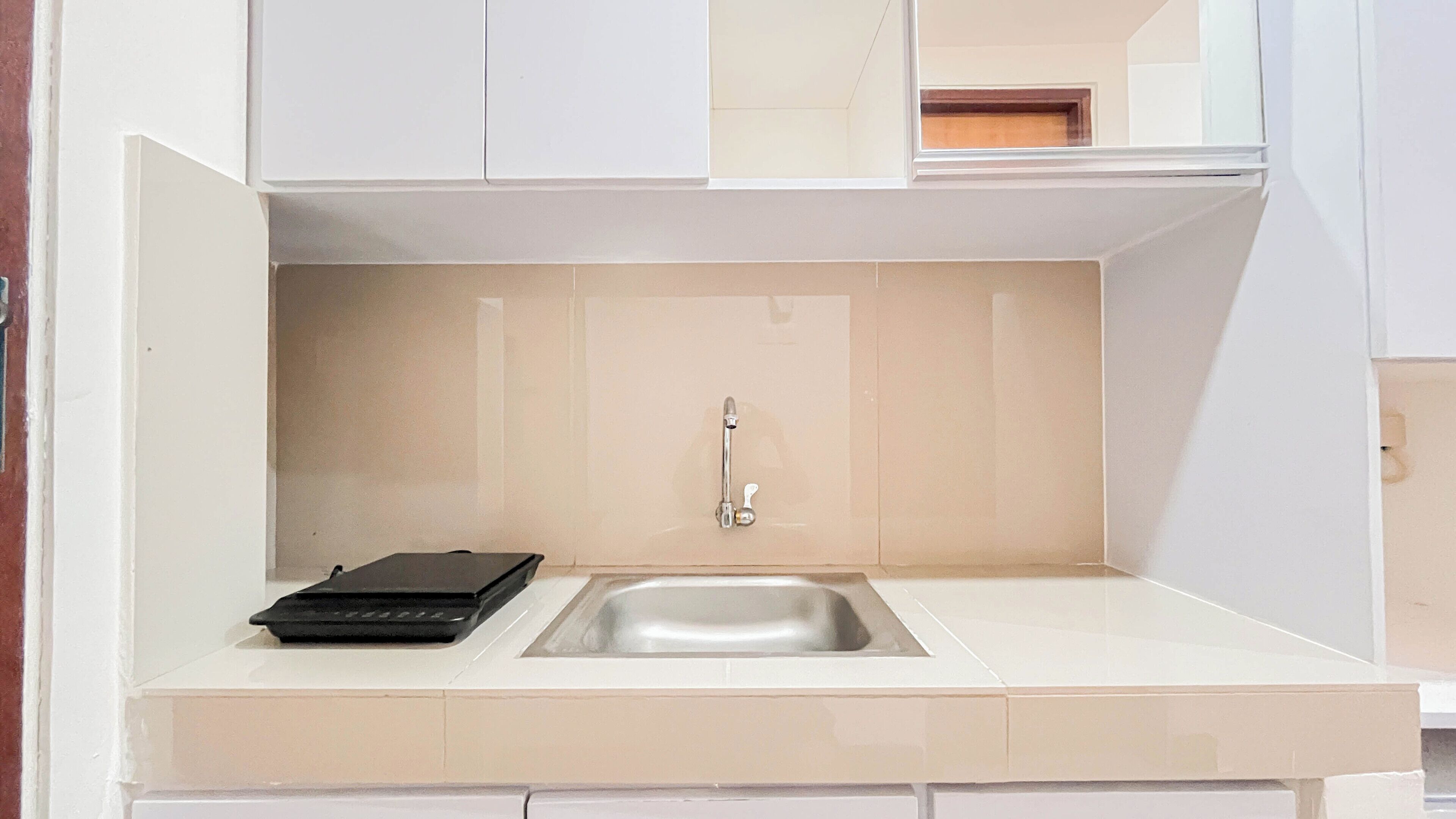 A compact kitchen with a sink, a small black appliance, and a beige backsplash.