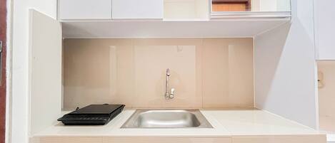 A compact kitchen with a sink, a small black appliance, and a beige backsplash.
