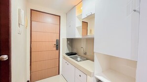 Cocina pequeña con puerta de madera, un lavabo y armarios blancos.