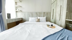 A neatly made bed with white linens, a wooden headboard, and a bedside table with a tray holding a book and a bottle.