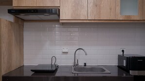 A kitchen with wooden cabinets, a black countertop, a stainless steel sink, and a black range hood. - Comfy Designed Studio Apartment At Anwa Residence (South Tangerang)