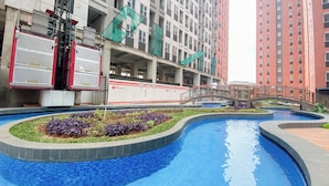 A swimming pool with a tiled edge, surrounded by a landscaped area with plants. - Comfortable Design Studio Room At Transpark Juanda Bekasi Timur Apartment (Bekasi)