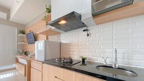 A modern kitchen with a black countertop, wooden cabinets, a stainless steel sink, and a built-in range hood. - Spacious And Comfy Studio Apartment Royal Sentul Park (Bogor)