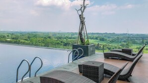 An infinity pool with lounge chairs and a view of a green landscape. - Spacious And Comfy Studio Apartment Royal Sentul Park (Bogor)