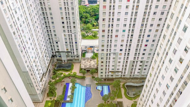 A high-rise residential building with multiple balconies, a central swimming pool, and surrounding greenery.
