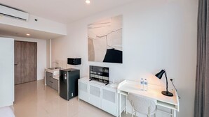 Een moderne, minimalistische kamer met een wit bureau, een stoel, een kleine kitchenette en een groot abstract schilderij aan de muur.