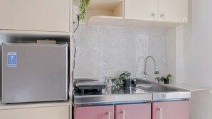 A compact kitchen with a refrigerator, sink, and pink cabinets. - Cozy Studio Apartment Bassura City (Jakarta)