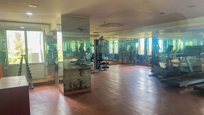 A gym with exercise equipment, large windows, and a wooden floor. - Cozy Studio Apartment Bassura City (Jakarta)