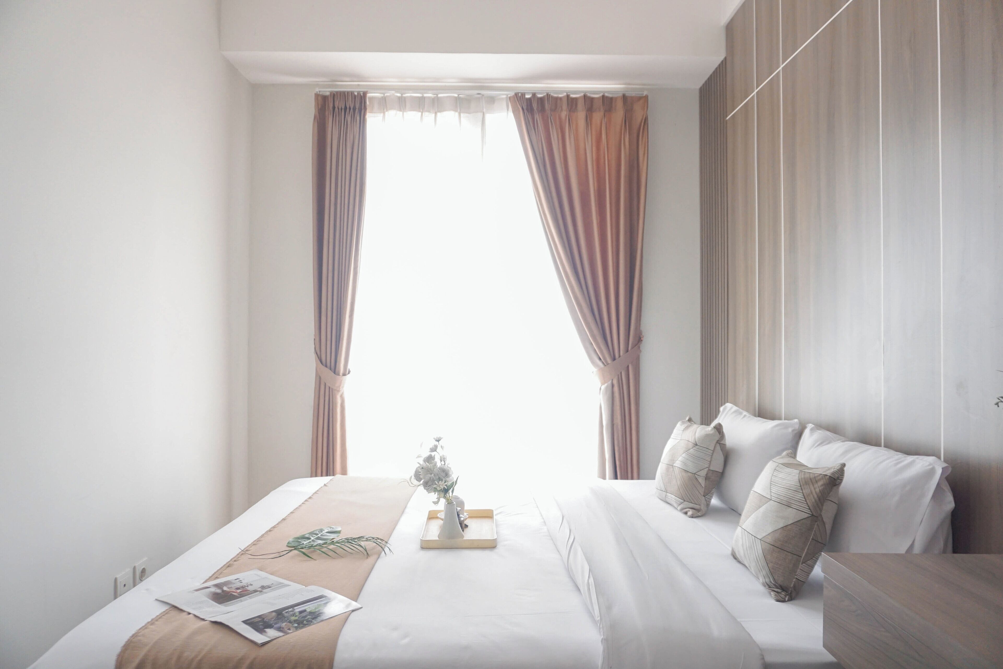 A modern hotel room with a large bed, a bedside table, and a window with curtains.