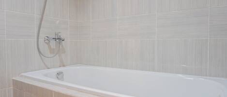 A modern bathroom with a freestanding bathtub, a showerhead, and tiled walls.