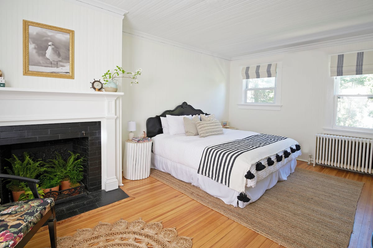 A bedroom with a fireplace, a bed with a black headboard, and a window with curtains.