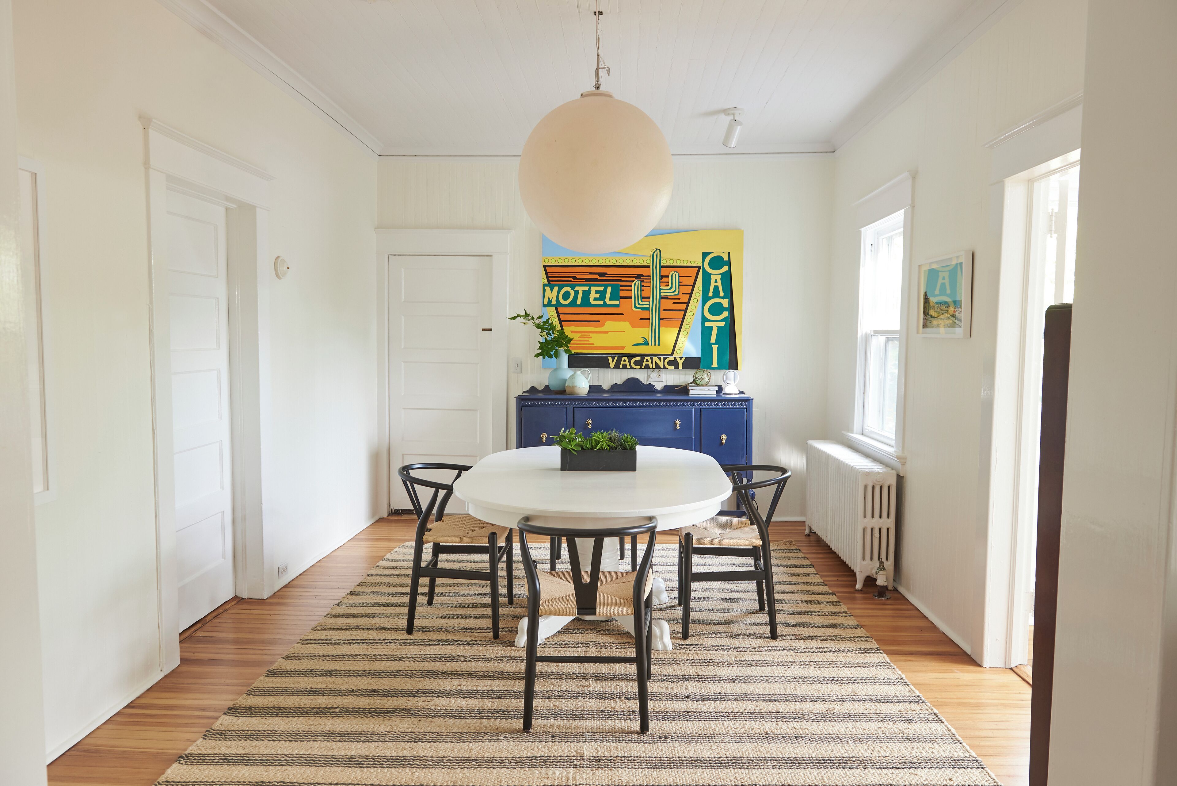 A dining area with a round table, six chairs, a hanging light fixture, a blue cabinet, and a radiator.