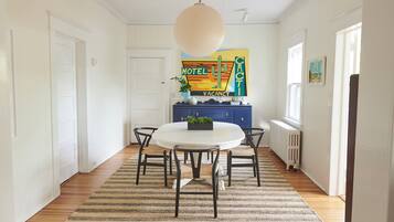 A dining area with a round table, six chairs, a hanging light fixture, a blue cabinet, and a radiator.