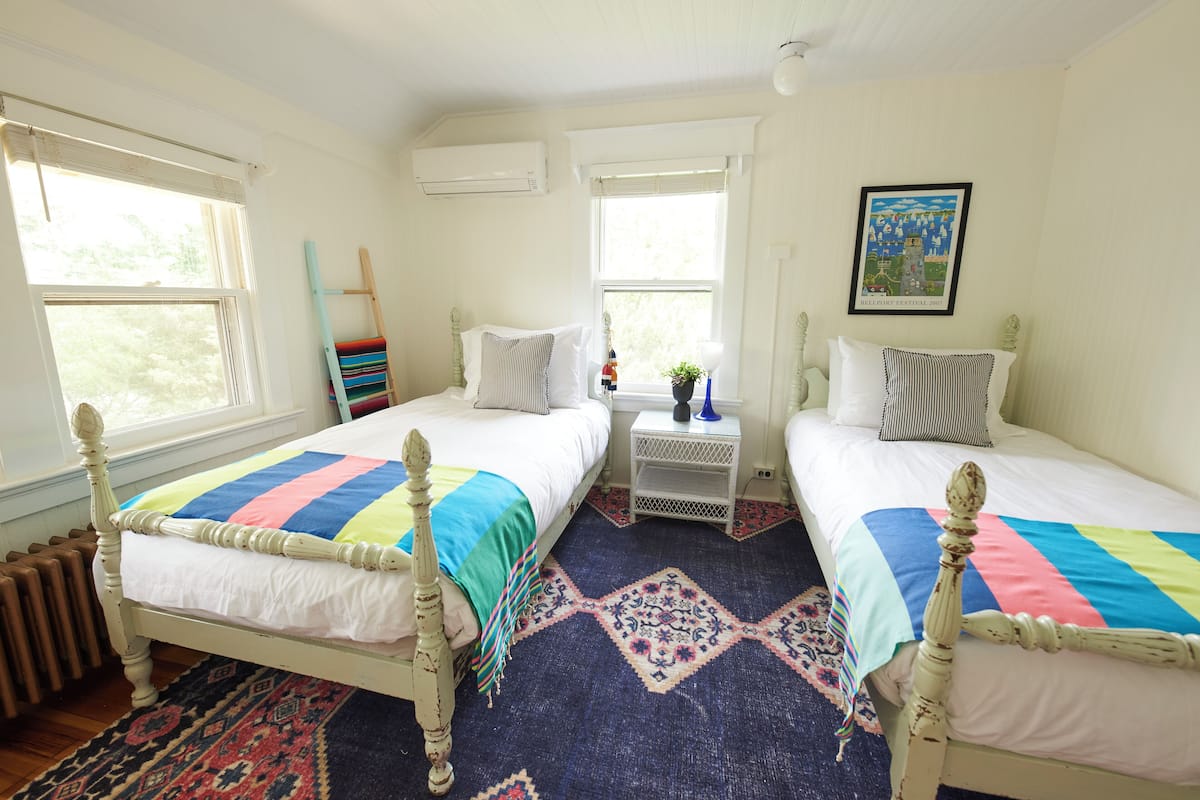 A bedroom with two beds, a window, a radiator, and a framed picture on the wall.