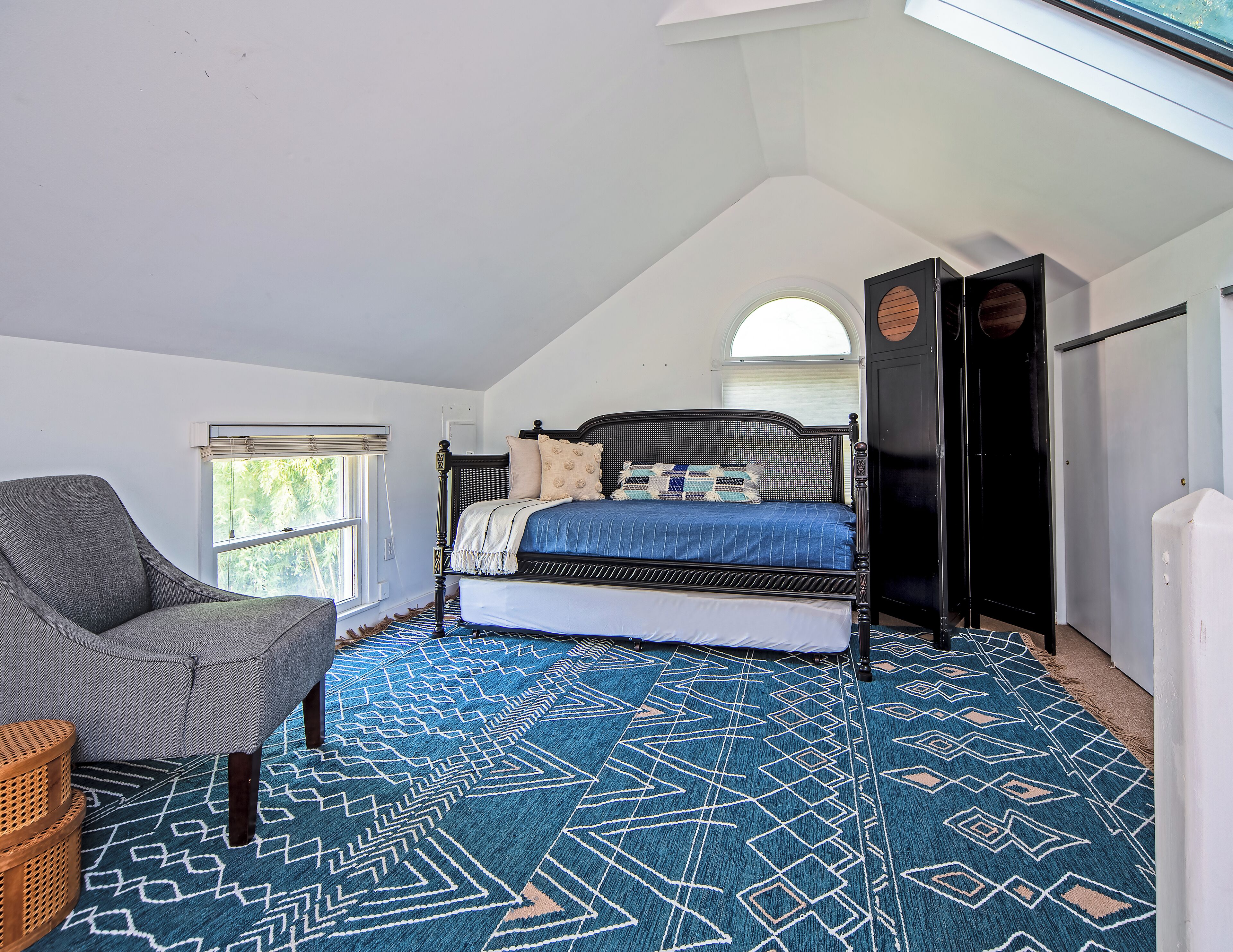 A bedroom with a bed, a chair, a window, and a patterned rug.