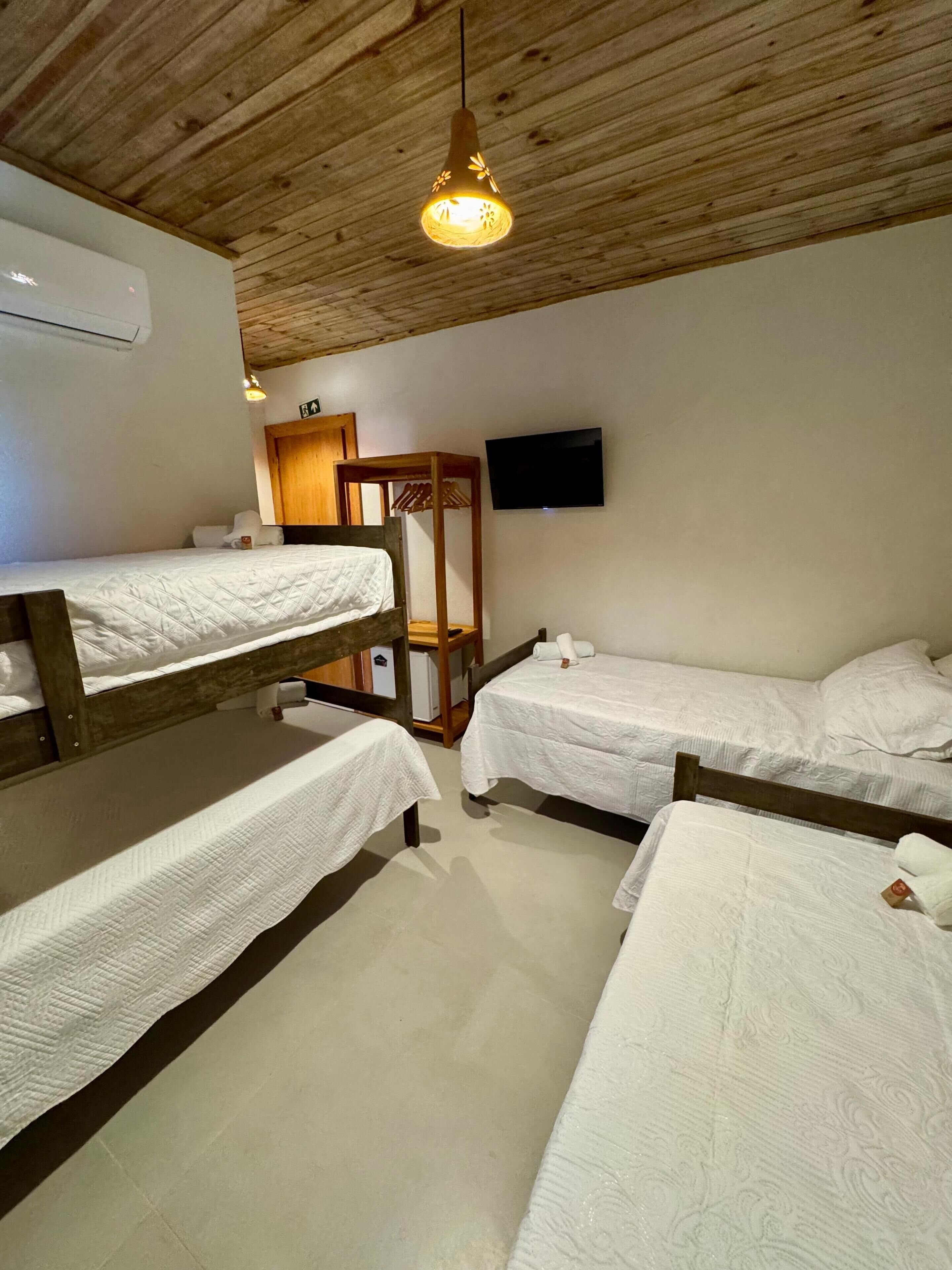 A room with bunk beds, a wooden ceiling, a television, and a wooden wardrobe.