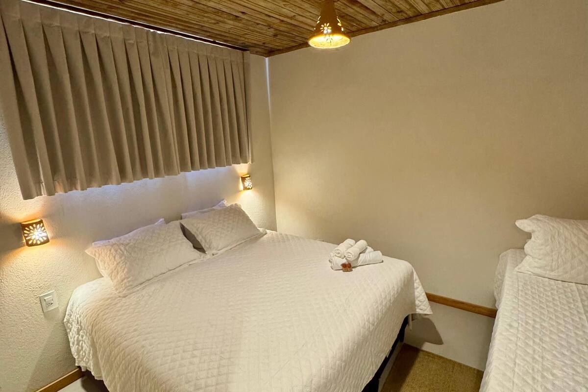 Ein Schlafzimmer mit Holzboden, einem Bett mit weißer Bettwäsche, einem Nachttisch mit Lampe und einem Fenster mit Jalousien.