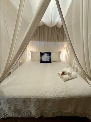 A bed with a canopy, pillows, and a rolled towel. - Caraiva Suites (Porto Seguro)