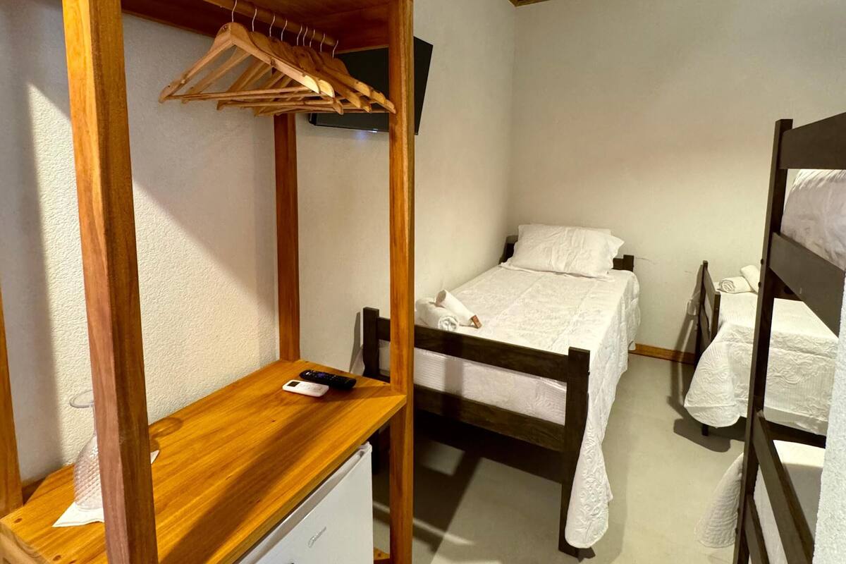 Ein kleines Zimmer mit einem Etagenbett, einer Holzregaleinheit mit Kleiderstange, einem kleinen Tisch und einer Fernbedienung sowie einer weißen Schublade.